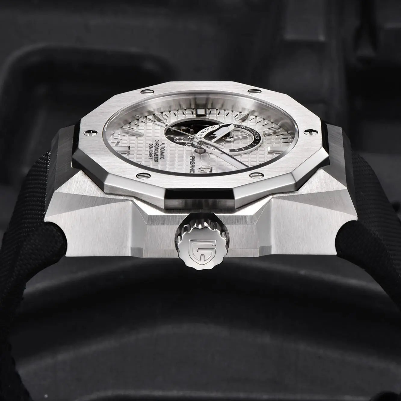 Close-up of a silver watch with a detailed face, held by a gloved hand.